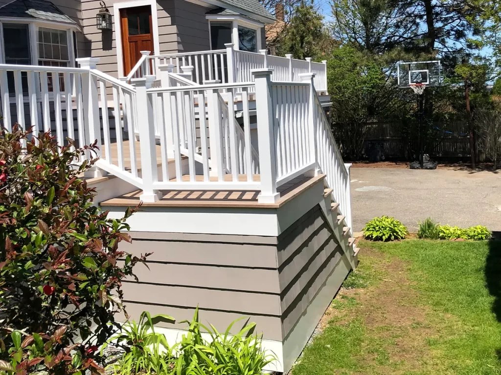 A refinished deck with white railings beside a painted home